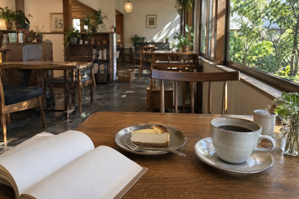 本とコーヒーとケーキを置いたカフェの窓辺の席（AI生成イメージ）